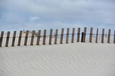 Wooden fence on beach against sky