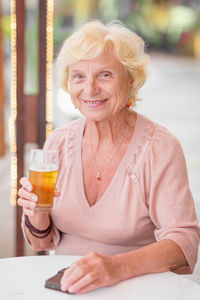 Mature woman sitting at a table in a summer cafe and drinking beer