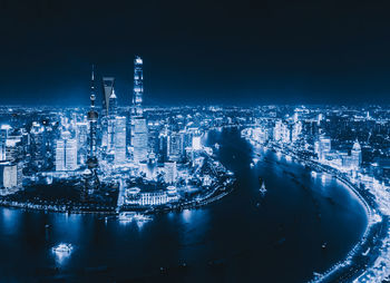 High angle view of illuminated city by sea against sky at night