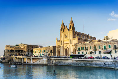 Buildings by river against blue sky