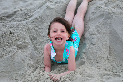 Portrait of smiling girl lying on sand at beach