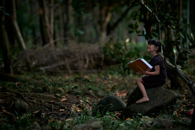 Little child reading a book in a green coastal forest