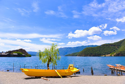 Boats moored on shore by lake against sky