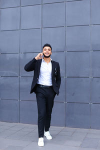 Full length of businessman talking on phone standing against wall