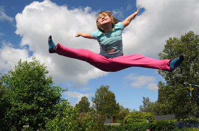 Low angle view of girl jumping over trees against sky