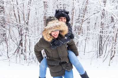 Portrait of young couple on snow covered tree during winter