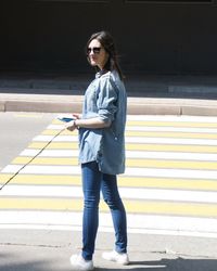 Young woman standing by crosswalk during sunny day