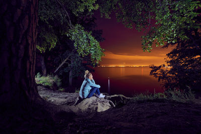 Woman sitting by lake at night