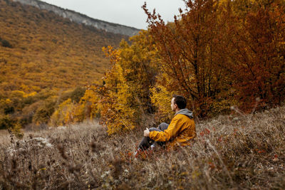 A young man in a yellow jacket admires the autumn mountain and forest landscape