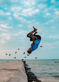 Young adult jumping in sea against sky