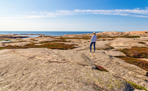 Man standing on rock by sea against sky