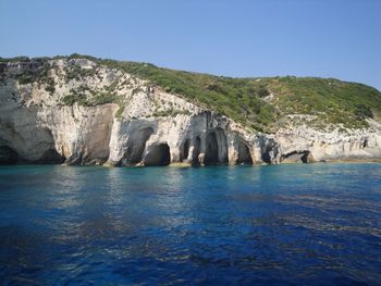 Scenic view of rocks by sea against clear blue sky