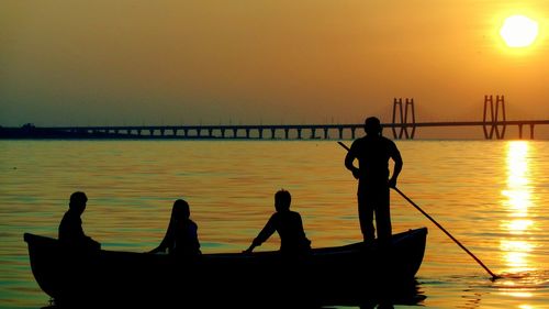 Silhouette people on boat in sea against sky during sunset