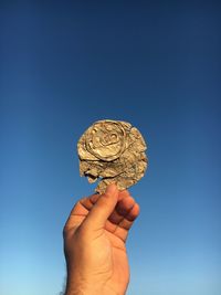 Cropped image of hand holding crushed drink can against clear sky