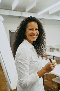 Side view portrait of smiling teacher with curly black hair standing by flipchart in classroom