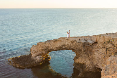 Man standing on rock by sea against sky