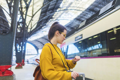 Side view of woman with luggage checking time while standing at railroad station platform