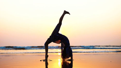 Side view of silhouette woman practicing yoga at beach during sunset