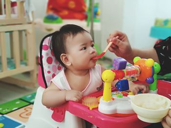 Cropped hand of mother feeding cute girl at home