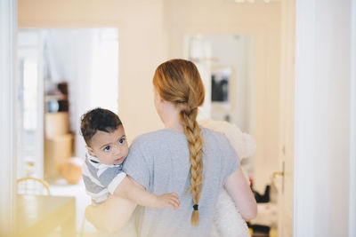 Rear view of mother with braided hair carrying son at home
