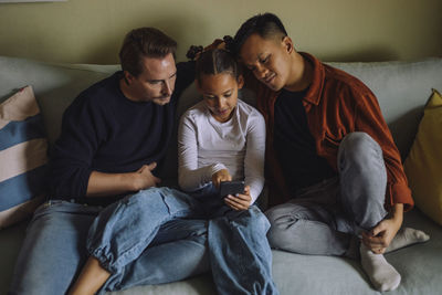 High angle view of gay couple sitting with daughter using smart phone while sitting on sofa at home