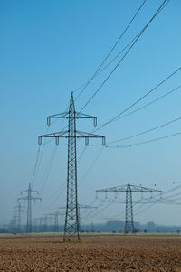 Low angle view of electricity pylon against clear blue sky