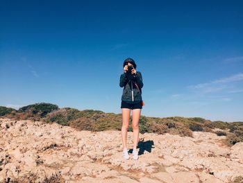 Woman standing on sand against blue sky