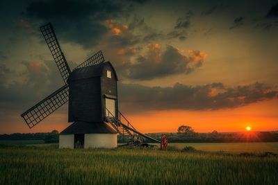 Traditional windmill on field against sky during sunset