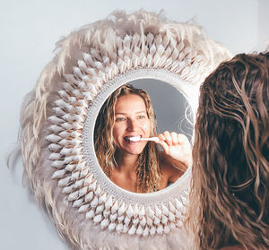 Reflection of beautiful woman brushing teeth seen through mirror