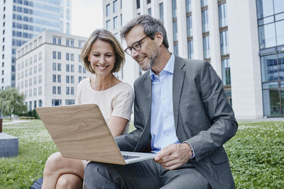 Smiling businesswoman and businessman sharing laptop outdoors