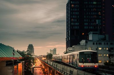 Illuminated street amidst buildings against sky at dusk