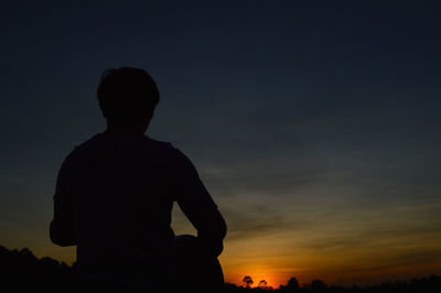 Rear view of silhouette boy standing against sky during sunset