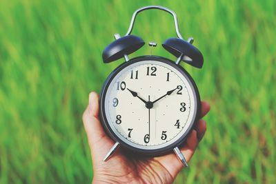 Close-up of hand holding clock against grassy field