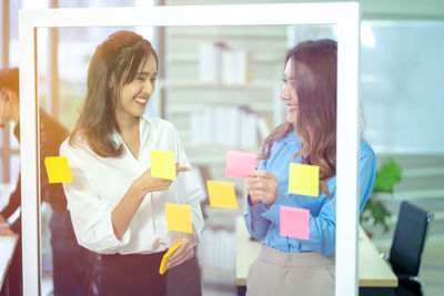 Young woman using phone while standing in office