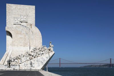 Seagulls on bridge over sea against blue sky