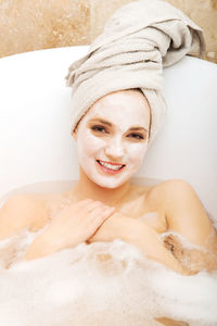 Portrait of smiling young woman with facial mask lying in bathtub at home