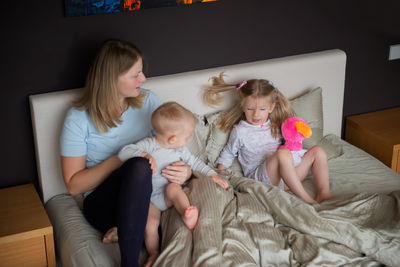 High angle view of mother with children sitting on bed at home