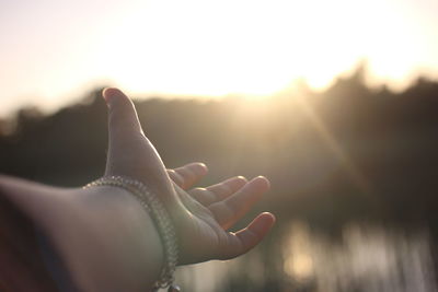 Close-up of hand against sun during sunset