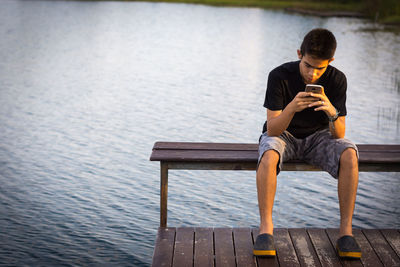 Young man using mobile phone while sitting on lake
