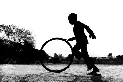 Silhouette man playing with tire against clear sky