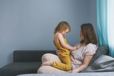 Plus, european mother hugs toddler child sitting on sofa in real interior of living room