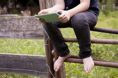 Low section of boy using tablet computer sitting on gate