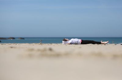 Side view of carefree girl lying at beach against sky during sunny day