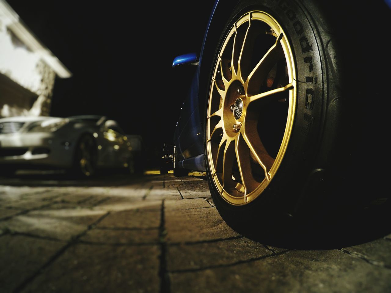 land vehicle, mode of transport, night, wheel, close-up, part of, selective focus, focus on foreground, outdoors, stationary, no people, cropped, illuminated