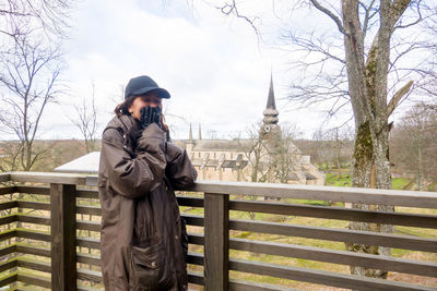 Man photographing on railing against sky during winter