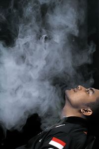 Side view of young man smoking while sitting against black background