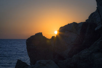 Rock formation in sea against sky during sunset