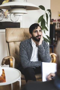 Thoughtful male patient discussing with therapist at home office