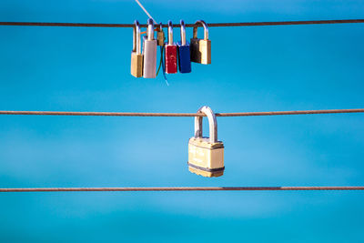 Low angle view of padlocks on steel cable against blue sky