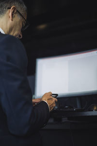 Low angle view of businessman using smart phone against computer at workplace